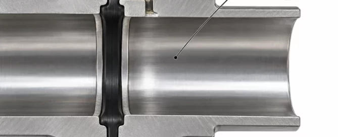Cutaway illustration of a powder-transfer connection showing a visibly clean exposed steel bore, one powder pocket in a recessed gasket groove with an open route to the bore, and a separate magnified inset of sparse particles attached to exposed steel.